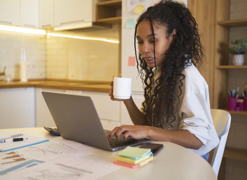 mulher negra sentada à mesa enquanto olha para a tela do computador