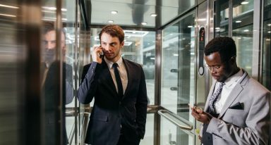 dois homens de terno posicionados como se analisassem algo, um fala ao telefone enquanto outro olha para o celular