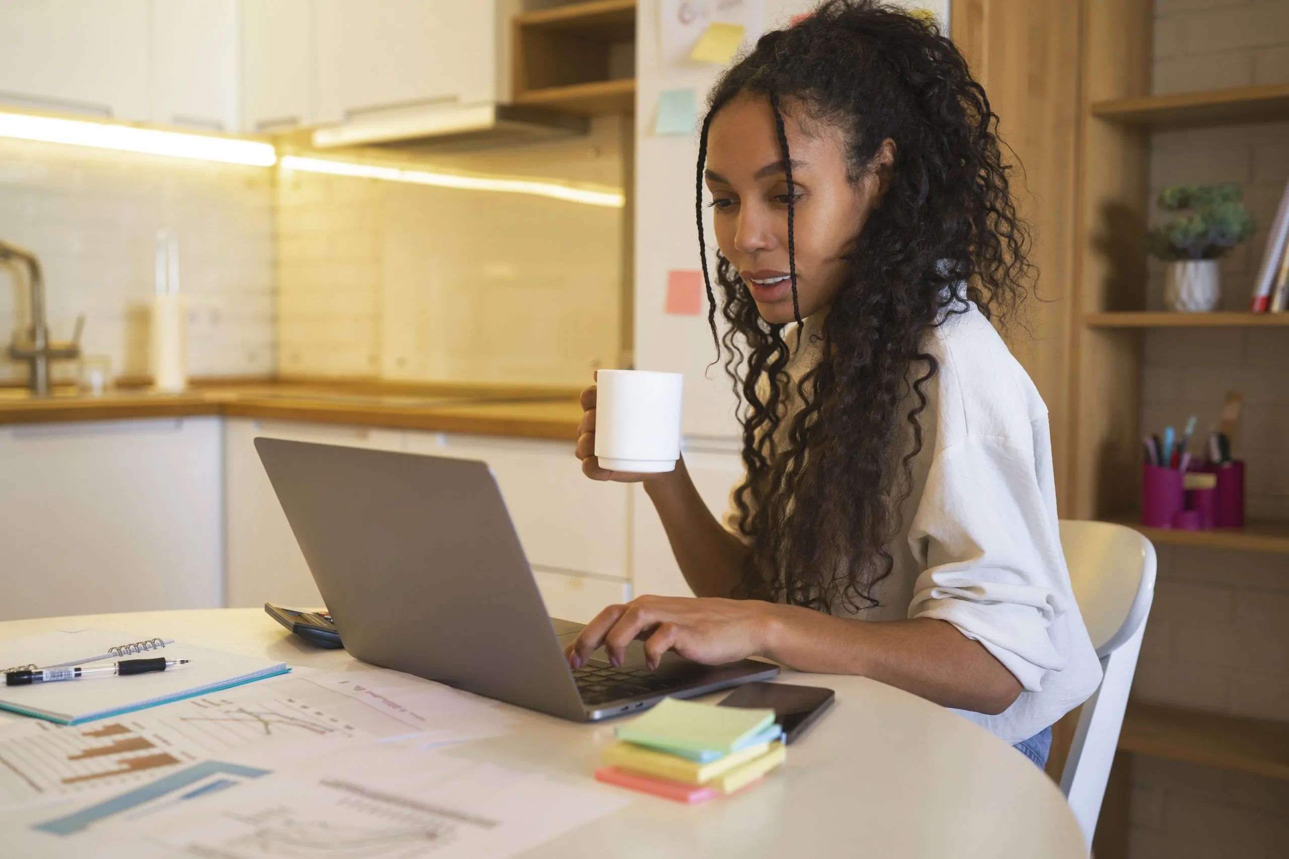 mulher negra sentada à mesa enquanto olha para a tela do computador