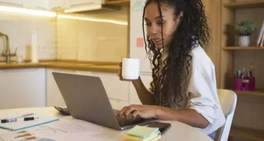mulher negra sentada à mesa enquanto olha para a tela do computador